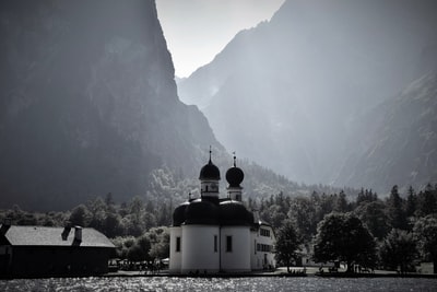 被群山环绕的水体附近小教堂的灰度照片